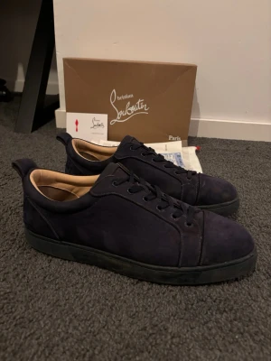 Mörkblå sneakers från Louboutin - Snygga mörkblå sneakers från Christian Louboutin i mocka med klassisk röd sula och svarta snören. Låg modell med stilren design och diskreta sömmar. Insidan är ljusbeige och sulan har Louboutin-loggan ingraverad.