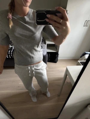 Grå stickad tröja med kort ärm - Säljer en stilren grå stickad tröja med korta ärmar och rund hals. Tröjan har en mjuk och följsam passform, perfekt för lager på lager eller som den är. Enkel men snygg design som passar till det mesta.