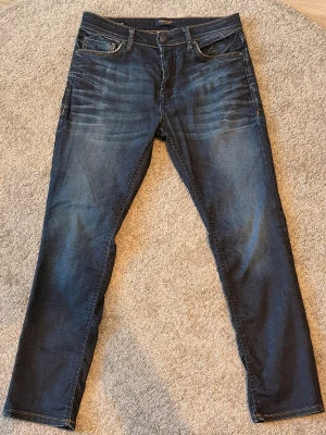 Mörkblå slim fit jeans från Jack & Jones - Snygga mörkblå slim fit jeans från Jack & Jones med klassisk femficksdesign och diskreta slitningar framtill. Jeansen har normal midja, raka ben och kontrastsömmar. Perfekta till en avslappnad stil och passar till det mesta.