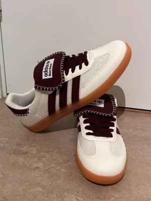 Adidas Samba OG vinröd/vit - Säljer ett par Adidas Samba OG sneakers i vitt och vinrött med klassiska tre ränder på sidan, gummisula och bred plös. Skorna har ovandel i mocka och läder, samt vinröda snören och detaljer. Perfekta för dig som gillar retrostil och streetwear.