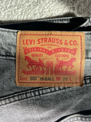 Grå Levi's 502 Hi-Ball jeans - Säljer ett par grå Levi's 502 Hi-Ball jeans med klassisk femficksdesign och rakt ben. Jeansen har en snygg tvättad look och den ikoniska röda Levi's-lappen på bakfickan. Perfekta för dig som gillar en avslappnad men stilren stil.