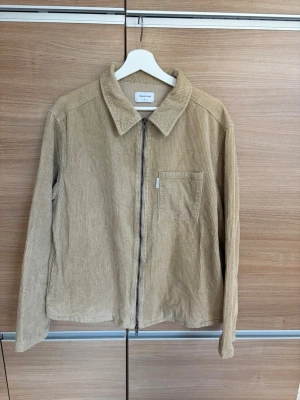 Beige overshirt i manchester - Stilren beige overshirt från Studio Total i mjuk manchester. Jackan har dragkedja framtill, klassisk krage och en bröstficka. Perfekt lager-på-lager-plagg med avslappnad passform och långa ärmar.