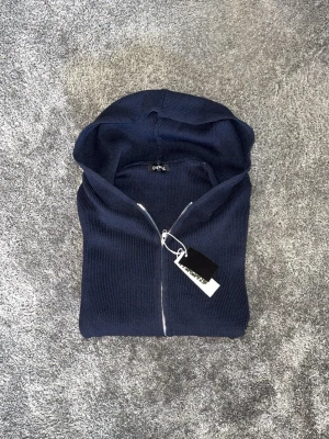Mörkblå zip up hoodie  - Snygg mörkblå hoodie från bycastello med dragkedja framtill och klassisk huva. Tillverkad i ett mjukt, ribbstickat material som känns skönt mot huden. Perfekt för dig som gillar streetwear och vill ha en stilren look.