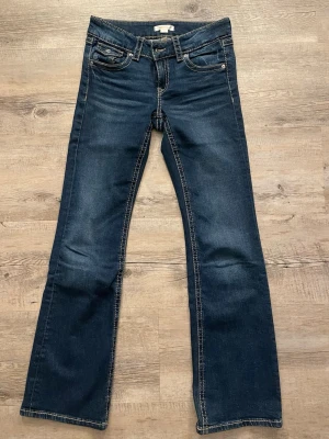 Mörkblå bootcut jeans med kontrastsömmar - Snygga mörkblå bootcut jeans med kontrastsömmar och klassiska fem fickor. Baksidan har fickor med lock och knappdetaljer. Jeansen har normal midja och är tillverkade i ett mjukt denimtyg som ger en bekväm passform.