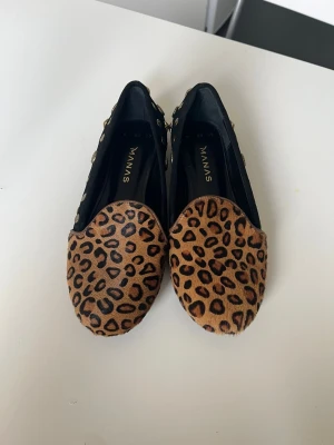 Leopardmönstrade loafers från Manas - Säljer ett par loafers från Manas med leopardmönstrad ovandel i brunt och svart. Skorna har svarta sidor dekorerade med guldiga nitar och stjärnor. Yttersulan är svart med hjärt- och rosettmönster. Perfekta för dig som vill sticka ut med din stil.