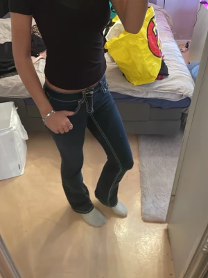Mörkblå bootcut jeans med vita sömmar - Snygga mörkblå bootcut jeans med markerade vita sömmar och låg midja. Klassisk femficksmodell och dragkedja med knapp framtill. Perfekta för en trendig och avslappnad look.
