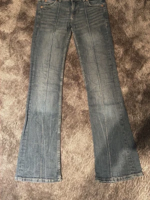 Blå bootcut jeans med pressveck - Säljer ett par blå bootcut jeans med markerade pressveck framtill. Jeansen har klassisk femficksdesign och är tillverkade i denim med lätt tvättad look. Perfekta för dig som gillar retrovibbar och vill ha ett par jeans med snygg passform.