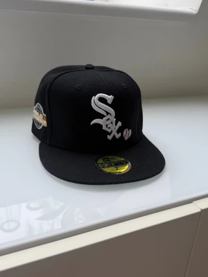 Svart White Sox keps New Era 59Fifty - Snygg svart keps från New Era 59Fifty med White Sox-logga broderad i vitt framtill och ett litet hjärta. Platt skärm och patch på sidan. Klassisk streetwear-stil, perfekt för dig som gillar sportiga accessoarer.
