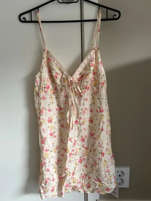 Blommig miniklänning från Miss Selfridge - Söt miniklänning med smala axelband från Miss Selfridge. Klänningen är ljus med blommigt mönster i rosa och grönt, har v-ringning och knyt framtill. Perfekt för varma dagar och somriga tillfällen.