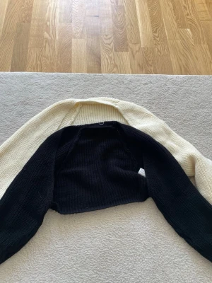 Svart och vit stickad bolero - Snygg stickad bolero i svart och vitt. Ärmarna och ryggen är svarta medan framsidan och axlarna är vita. Perfekt att slänga över en topp för en cool lager-på-lager-look.