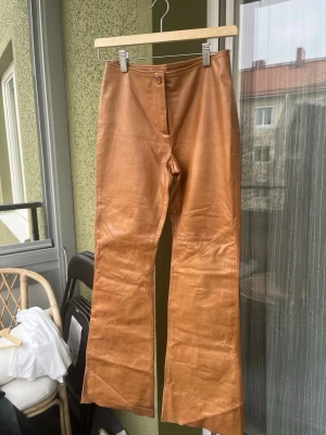 Bruna bootcut byxor i skinn - Snygga bruna byxor i äkta skinn med bootcut-modell och hög midja. Byxorna har en klassisk knappstängning framtill och är perfekta för dig som vill sticka ut med en cool och trendig look. Har några fläckar, se bild.