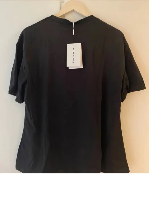 Svart Acne Studios t-shirt Stockholm - Svart t-shirt från Acne Studios med tryck 'Acne Studios STOCKHOLM 1996' på bröstet. Klassisk rund hals och korta ärmar. Tillverkad i mjuk bomull för en skön och avslappnad look.