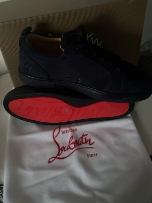 Navy blåa CL sneakers - Snygga blåa sneakers från CL med ikonisk röd sula och diskret logga på sidan. Skorna har lågt skaft, blåa snören och är tillverkade i en mix av läder och mocka. Perfekta för dig som vill ha något exklusivt och stilrent. Tveka inte om att höra av