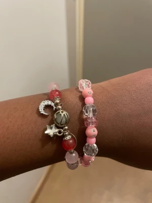 Två rosa pärlarmband med berlocker - Två armband med pärlor i rosa, rött och silver. 