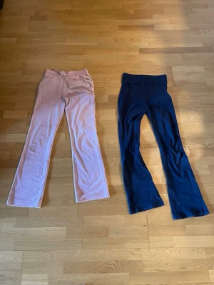 Två par mjukisbyxor i rosa och blå - Två par mjukisbyxor i mjukt velourmaterial, ett par i ljusrosa och ett par i mörkblått. Båda har utsvängda ben och bred resår i midjan för extra komfort. Perfekta för en avslappnad och trendig stil.