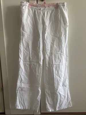 Vita linnebyxor från Gina Tricot - Snygga vita linnebyxor från Gina Tricot med rak passform och resår i midjan. Byxorna är tillverkade i ett lätt och luftigt linnematerial, perfekta för en avslappnad och trendig stil. Passar dig som gillar bekväma och stilrena plagg.