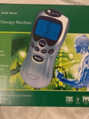 Digital Therapy Machine med display - Elektronisk terapimaskin med blå LCD-skärm, flera knappar och tillbehör som elektrodpads och sladdar. Silverfärgad plast, kompakt och smidig design. Perfekt för muskelavslappning och massage. Manual och originalförpackning medföljer.