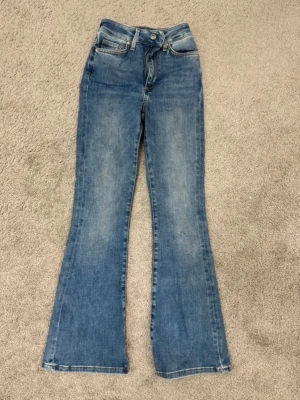 Blå utsvängda jeans i storlek S - Säljer ett par blå jeans med utsvängda ben och klassisk femficksdesign. Jeansen har normal passform och är tillverkade i denim. Perfekta för dig som gillar en retroinspirerad look.