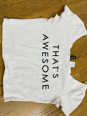 Vit t-shirt med tryck från Divided - Vit t-shirt från Divided med svart texttryck 'THAT'S AWESOME' på framsidan. Klassisk rund hals och korta ärmar. Tillverkad i mjuk bomull, perfekt för en avslappnad och trendig stil.