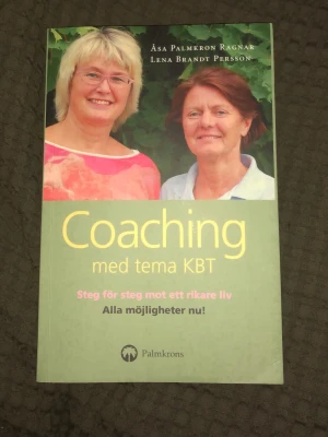 Coaching med tema KBT - Boken 'Coaching med tema KBT' av Åsa Palmkrons Ragnar och Lena Brandt Persson kombinerar klassisk coaching med modern KBT. Omslaget är grönt med gul text och har ett foto på två personer. Perfekt för dig som vill utvecklas och hitta nya möjligheter i livet.