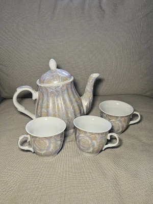 Blommigt tekanna och kopp-set - Säljer ett set med tekanna och tre koppar i porslin med lila och gult blommönster. Tekannan har lock och klassisk form, kopparna har matchande mönster och bekvämt handtag. Perfekt för teälskare som vill ha något unikt och stilrent i köket.