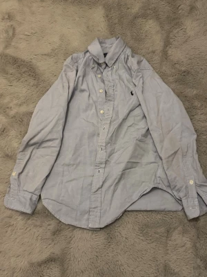 Ralph Lauren skjorta xs - Säljer ljusblå Ralph Lauren skjorta i Stl 10-12y som motsvarar 152cm men passar max upp till 160cm inte längre. Den är i superskick men inte strycken som ni kanske ser. Hör av er vid funderingar