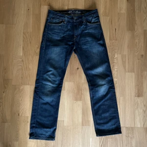 Mörkblå Levi's 501 jeans straight fit - Klassiska mörkblå Levi's 501 jeans med rak passform och fem fickor. Jeansen har en snygg tvätt med slitningar och kontrastsömmar. Tillverkade i kraftig denim med knappgylf och läderpatch bak i midjan. Perfekta för en avslappnad och tidlös stil.