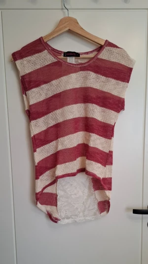 Randig topp från Annabelle i S - Säljer en luftig och cool topp från Annabelle i storlek S. Toppen är randig i rött/rosa och vitt, har en längre bakdel med spetsdetalj och är ärmlös. Perfekt för dig som gillar en avslappnad och trendig stil.