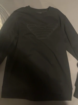  sweatshirt Emporio Armani - Snygg svart sweatshirt från Emporio Armani med det klassiska logotrycket på bröstet. Tröjan har rund halsringning och långa ärmar, perfekt för en stilren och enkel look.