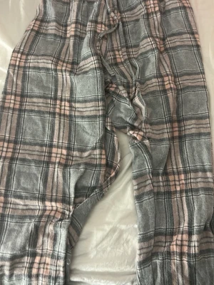 Rutiga pyjamasbyxor i grått och rosa - Mysiga pyjamasbyxor med rutigt mönster i grått, rosa och vitt. Byxorna har resår i midjan och är gjorda i ett mjukt, bekvämt tyg som passar perfekt för hemmakvällar. Klassisk avslappnad passform och långa ben.