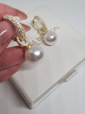 Guldörhängen med pärlor - Eleganta örhängen i guldton med gnistrande stenar och stora vita pärlor. Örhängena har en lyxig känsla och är perfekta för att lyfta vilken outfit som helst. Märket Lily and Rose syns på asken. Säljs som ett par.