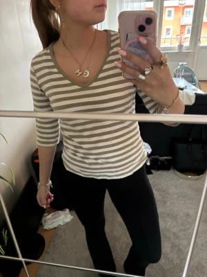 Randig v-ringad topp i bomull - Beige och vit randig topp med v-ringning och trekvartsärm. Tillverkad i mjuk bomull, perfekt för en avslappnad och stilren look. Passformen är normal och toppen är enkel att matcha med olika outfits.