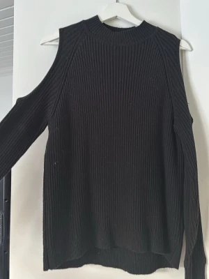 Svart stickad tröja med öppna axlar - Trendig svart stickad tröja med ribbad struktur och snygga shoulder-detaljer.