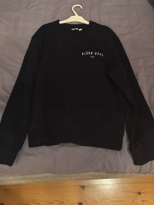 Svart sweatshirt från Björn Borg - En svart sweatshirt från Björn Borg med rund halsringning och diskret logga på bröstet. Tröjan har en klassisk passform med långa ärmar och ribbade muddar. Perfekt för en avslappnad och stilren look.