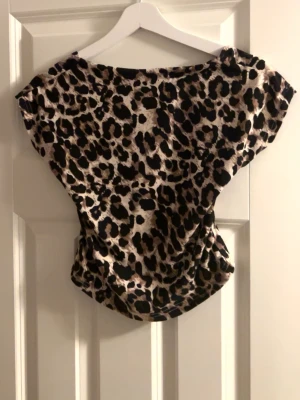 Leopardmönstrad croppad topp - Snygg croppad topp med leopardmönster. Toppen har korta ärmar och bred halsringning, vilket ger en avslappnad och trendig look. Perfekt för dig som vill sticka ut lite extra. Materialet känns mjukt och stretchigt. Har en öppen rygg som gör toppen till de lilla extra! Köpt tidigare på Plick men ursprungligen från shein. 