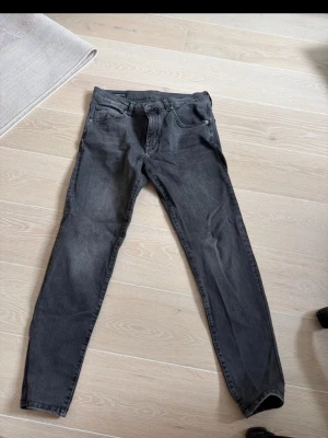 Svarta slim fit jeans från J.Lindeberg - Säljer ett par svarta slim fit jeans från J.Lindeberg med klassisk femficksdesign och dragkedja. Passar perfekt till en modern stil. 32/34