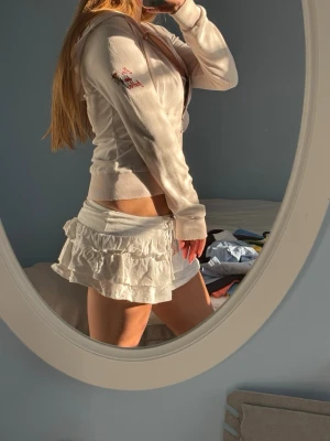 Beige hoodie med broderad detalj - Snygg beige hoodie med dragkedja och huva. Broderad detalj på ärmen ger en extra touch. Modellen är figurnära med ribbade muddar och passar perfekt till en avslappnad stil. Materialet känns mjukt och bekvämt mot huden.