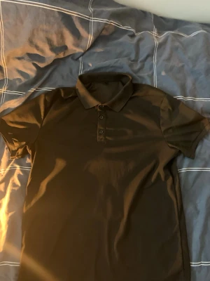 Svart piké t-shirt med krage - Säljer en svart piké t-shirt i storlek M. Tröjan har klassisk krage, knappar framtill och korta ärmar. Materialet känns mjukt och andas bra, perfekt till vardagslooken. Enkel och stilren design utan tryck eller mönster.