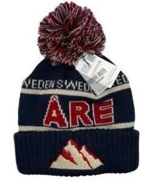 Mörkblå Åre mössa med tofs - Snygg mörkblå mössa med stor rödvit tofs på toppen. Framtill står det 'ÅRE' i rött och vitt, och nedtill finns ett broderat bergmotiv. Mössan har även texten 'SWEDEN' runt om och är stickad i mjukt material.