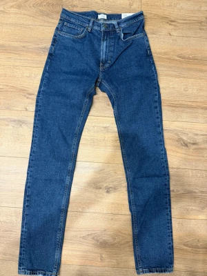 Mörkblå raka jeans - Säljer ett par klassiska mörkblå jeans med rak passform och fem fickor. Jeansen har normal midja och stängs med dragkedja och knapp. Tillverkade i slitstark denim, perfekta för en avslappnad och tidlös stil. STORLEK 29-32