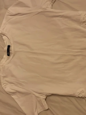 Vit t-shirt med spetsdetalj H&M - Vit t-shirt från Zara med rund halsringning och korta ärmar. Nedtill finns en snygg spetsdetalj som ger en extra touch. Tillverkad i mjuk bomull, perfekt för en enkel och stilren look.