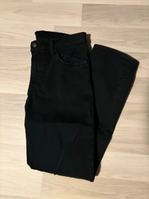 Svarta Levi's jeans med rak passform - Svarta jeans från Levi's med klassisk femficksdesign och rak passform. Jeansen har en diskret röd Levi's-tag på bakfickan och svart läderpatch i midjan. Perfekta för en clean och stilren look. Materialet är bomull med stretch för extra komfort. Storleken är W33 L31