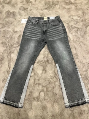 Flared Gallery Dept Jeans - Snygga grå jeans från Gallery Dept. med cool tvättad look och kontrasterande ljusare paneler längs benen. Klassisk femficksmodell med raka ben och råa kanter nertill. Perfekta för dig som gillar streetwear och unik stil.