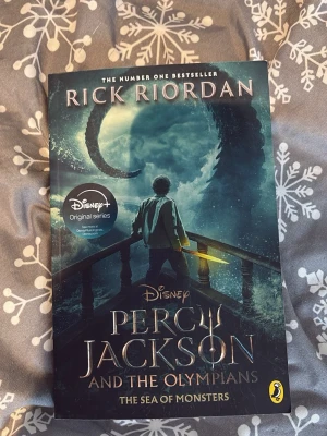 Percy Jackson: The Sea of Monsters - Säljer boken 'Percy Jackson and the Olympians: The Sea of Monsters' av Rick Riordan. Omslaget är mörkt med blå och gröna nyanser, motiv av Percy med ett svärd och ett havsmonster. Mjukpärm, engelska, fantasy och äventyr. Perfekt för dig som gillar spännande ungdomslitteratur.