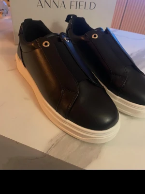 Svarta sneakers från Anna Field - Stilrena svarta sneakers från Anna Field med chunky vit sula och slät ovandel i konstläder. Skorna har metallöljetter och elastisk snörning för enkel påtagning. Perfekta för dig som gillar minimalistisk och modern look.