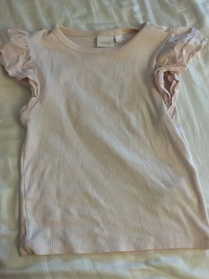 Ljusrosa ribbad topp från Gina Tricot - Supersöt ljusrosa topp från Gina Tricot med ribbad struktur och korta puffärmar med broderade detaljer. Perfekt för dig som gillar en feminin och trendig stil. Materialet känns mjukt och bekvämt mot huden.