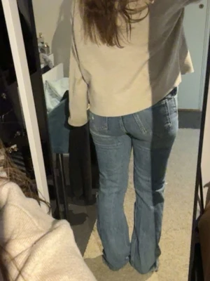 Blå bootcut jeans med slitningar - Säljer ett par blå bootcut jeans med slitningar på knäna och nedtill. Jeansen har klassisk femficksdesign och är i ett mjukt denimtyg. Perfekta för en avslappnad och trendig look.
