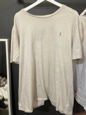 Beige t-shirt från Ralph Lauren - Klassisk beige t-shirt från Ralph Lauren med diskret logga broderad på bröstet. T-shirten är kortärmad och har en avslappnad passform.  Lite smutsig som du ser på bild 2