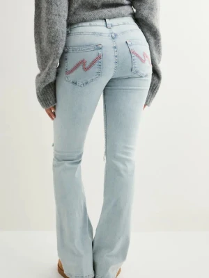 Ljusblå bootcut jeans med slitningar - Säljer ett par ljusblå bootcut jeans med slitna detaljer över knäna och broderade fickor bak i rosa och rött. Jeansen har hög midja och klassisk femficksdesign. Perfekta för en avslappnad och trendig look.
