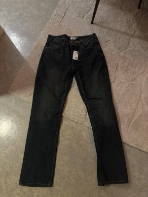 Nya jeans (icon) - Säljer ett par svarta jeans från lager 157 med rak passform och klassisk femficksdesign. Jeansen har en enkel look utan slitningar och är tillverkade i ett kraftigt denimtyg. Perfekta för dig som gillar en clean och stilren stil.